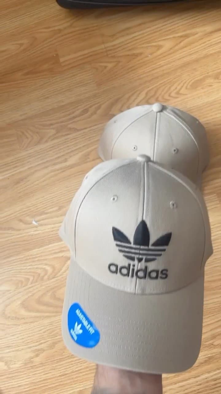 Gorra adidas gris con logo Trefoil negro bordado, ajustable, foto de producto sobre piso de madera
