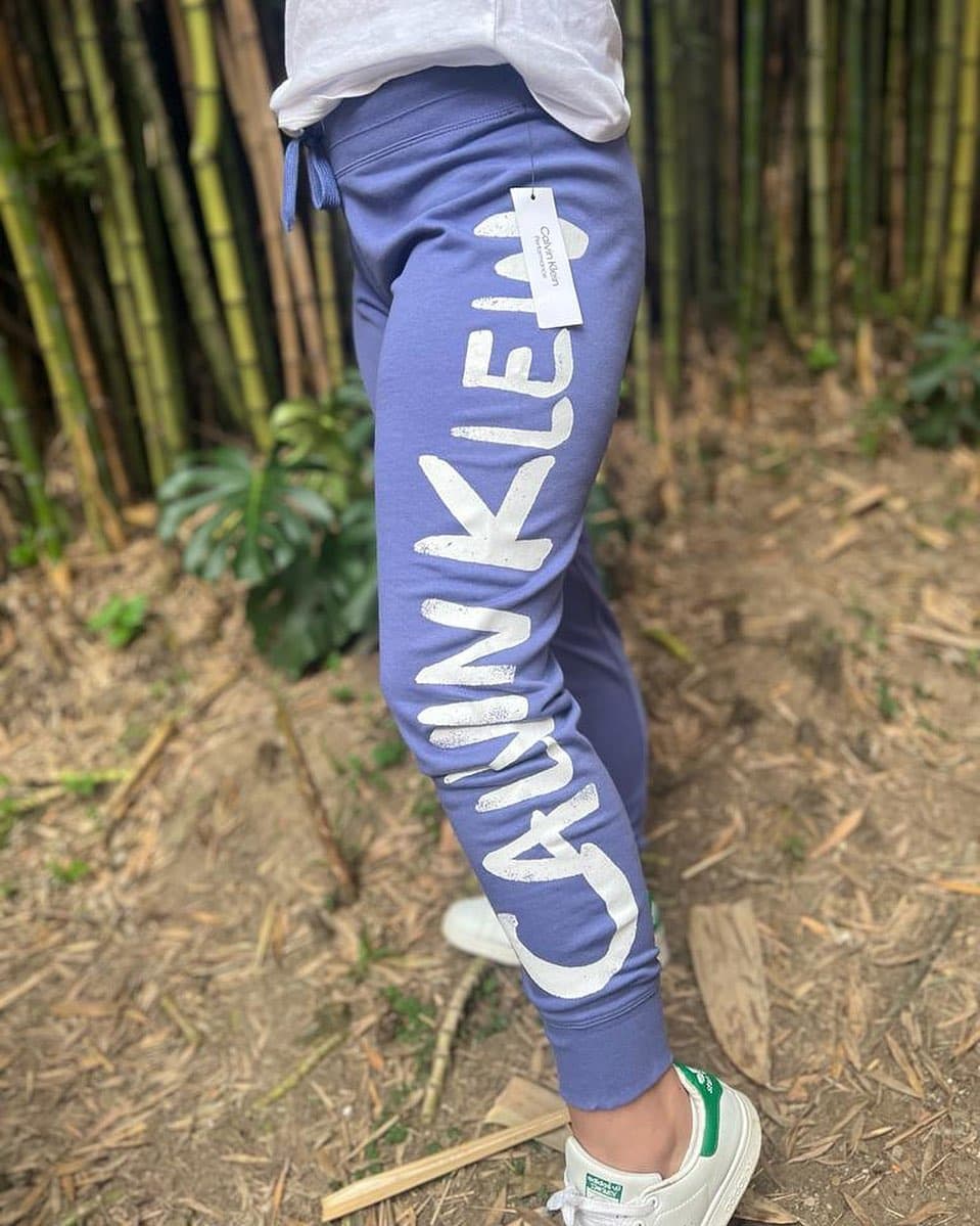 Jogger Calvin Klein Performance azul lavanda con logo blanco gigante en la pierna y etiqueta de papel colgando, en modelo